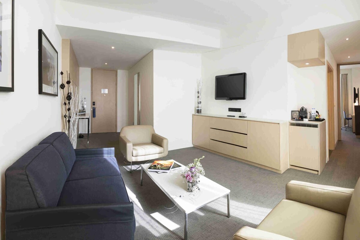 Un salon moderne comprenant un canapé, un fauteuil, une table basse, un téléviseur et un coin cuisine.