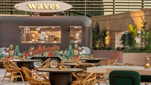 A food truck named 'Waves' with a 'California' theme, serving food in an outdoor dining area with wicker chairs and tables.