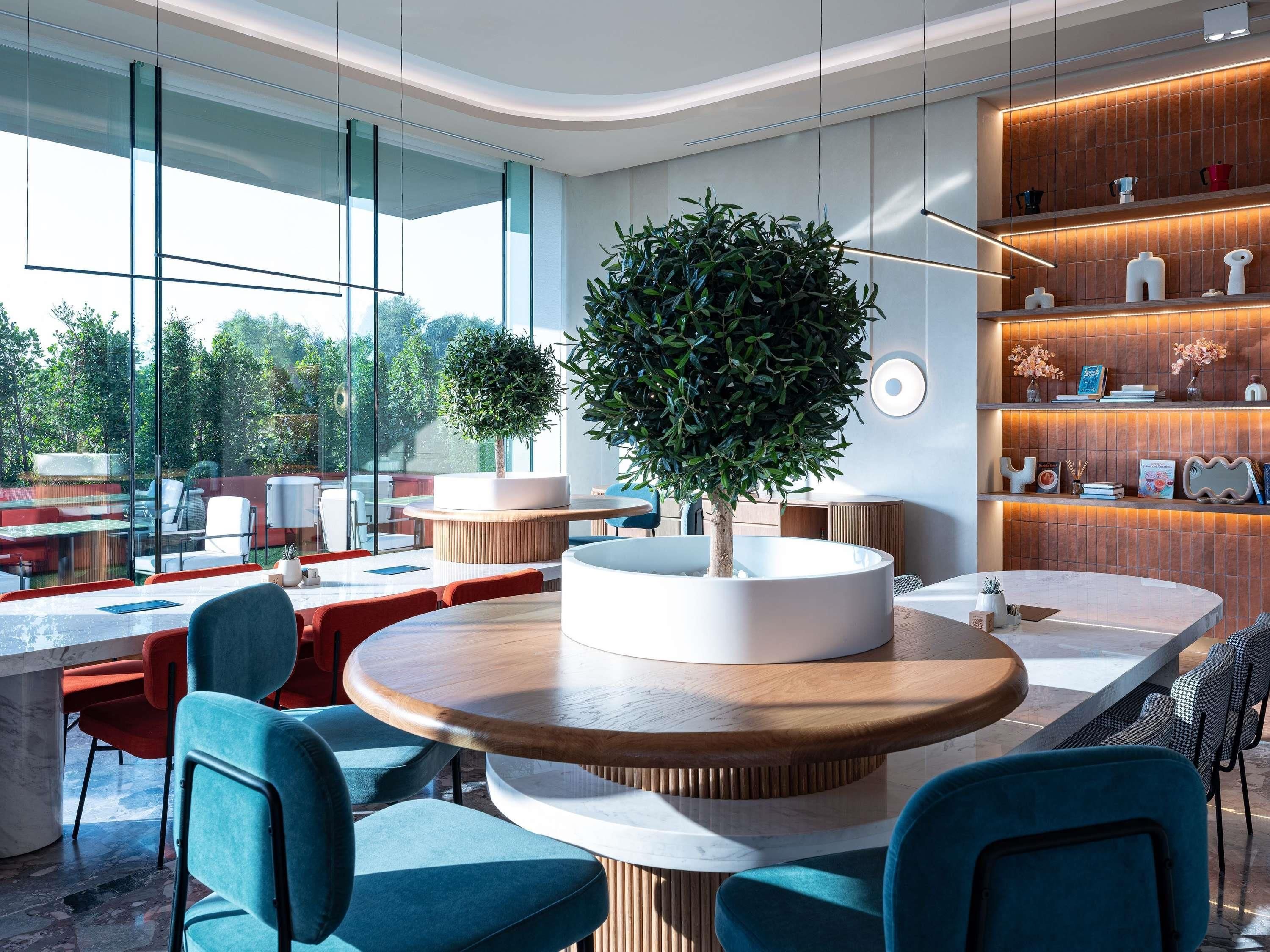 Un intérieur moderne avec des tables rondes, des chaises de couleur turquoise et un grand pot à plantes placé au centre.