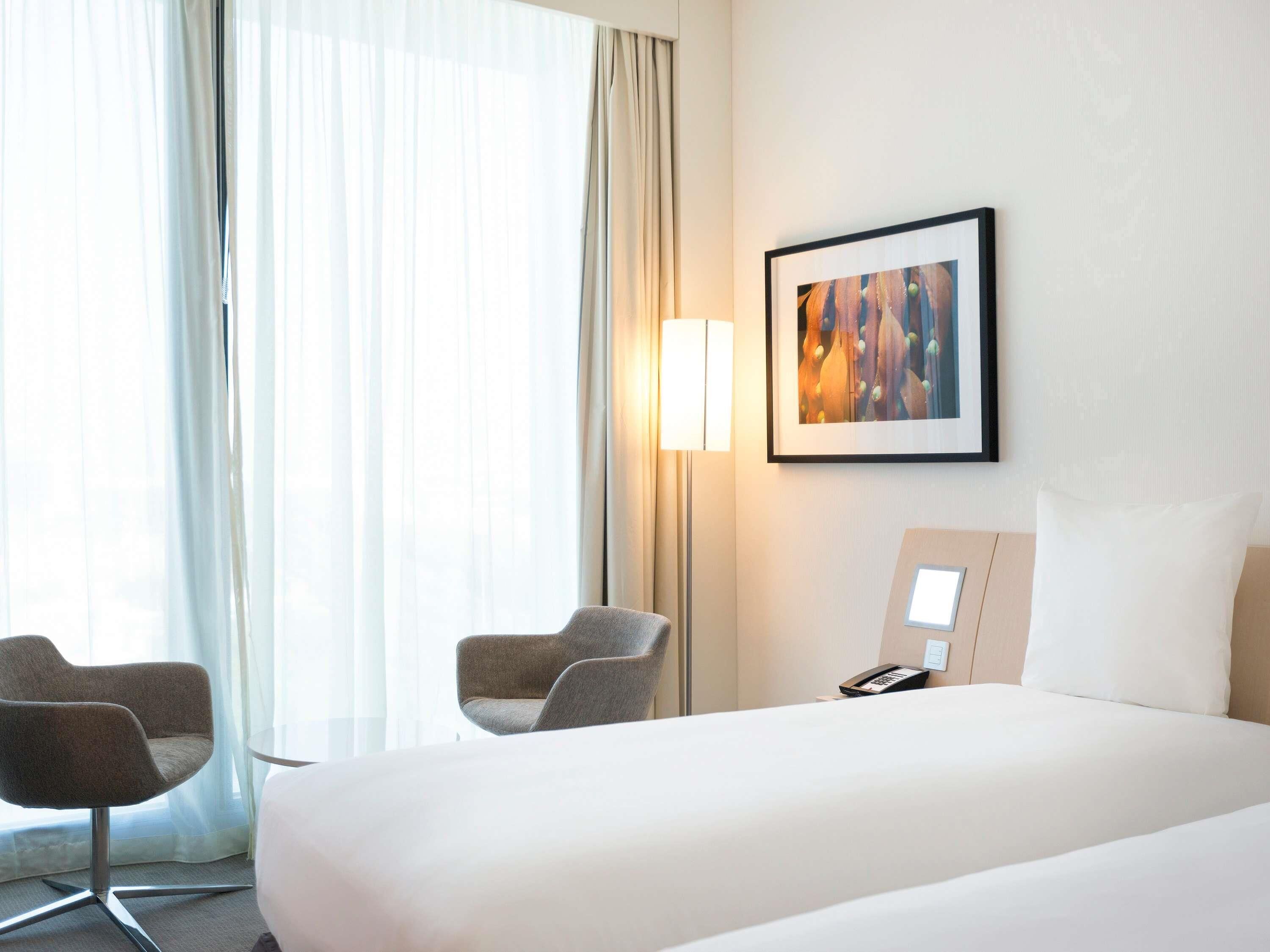 Een hotelkamer met een bed, twee fauteuils, een nachtkastje met telefoon, een lamp en een lijst aan de muur.