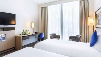 A hotel room with a large bed, a desk with a chair, a television, and a window with curtains.