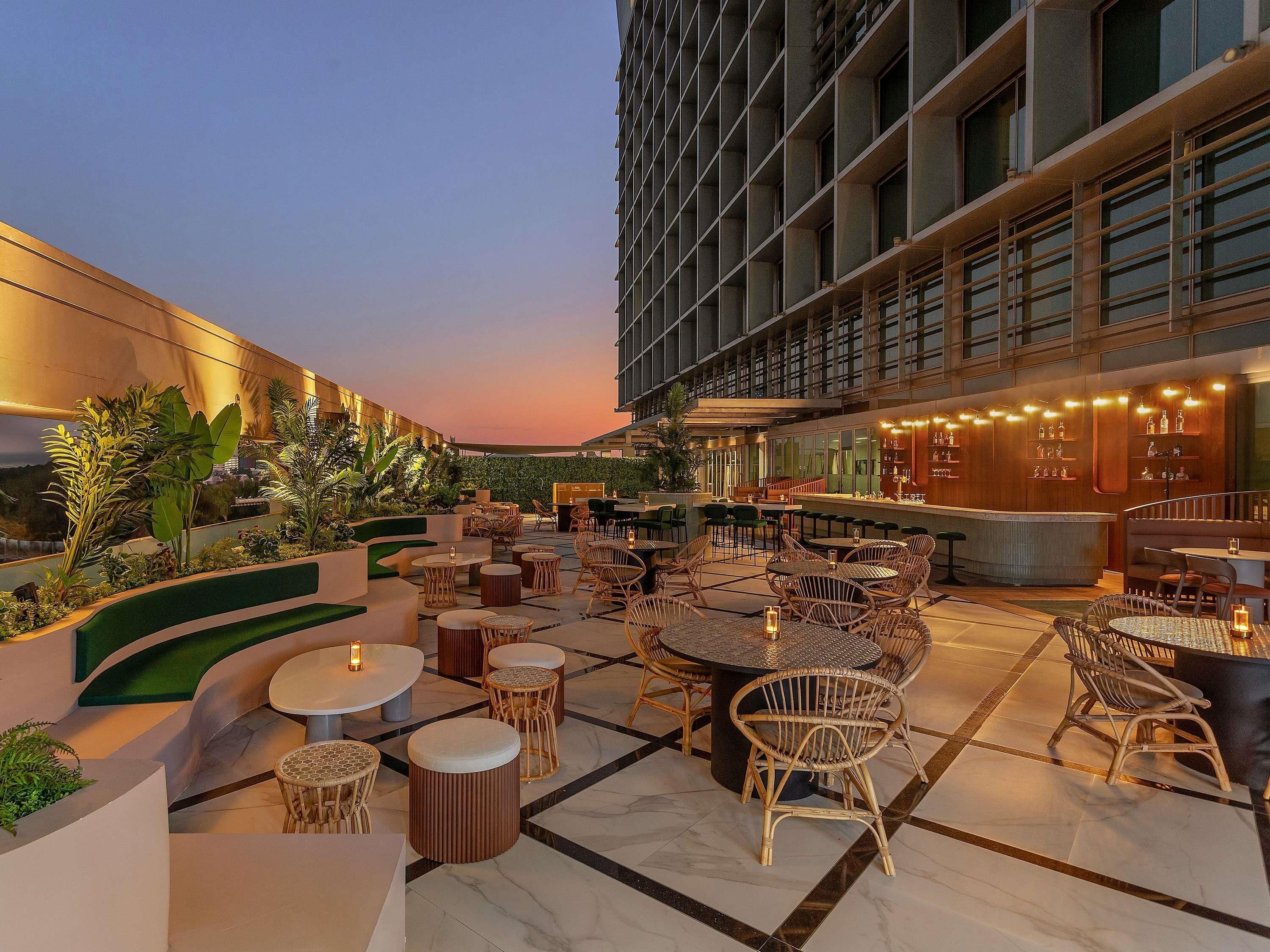 An outdoor seating area with tables and chairs, a bar, and a building with large windows.