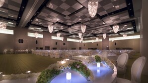 Een feestzaal met ronde tafels, witte stoelen en kroonluchters.