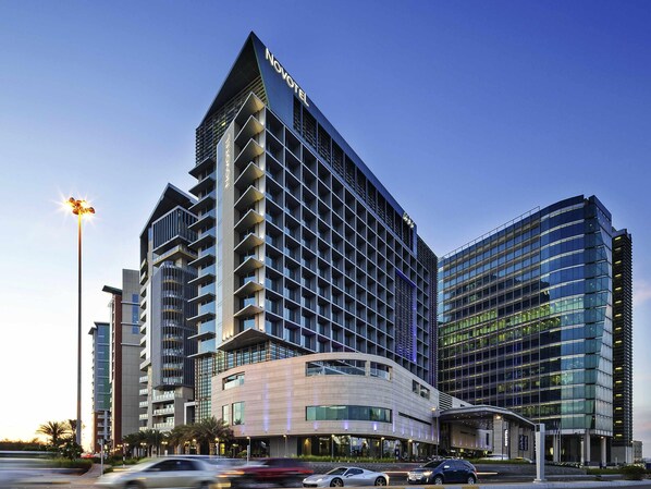 A modern hotel with a prominent 'Novotel' sign, multiple floors, and a mix of glass and concrete architecture.