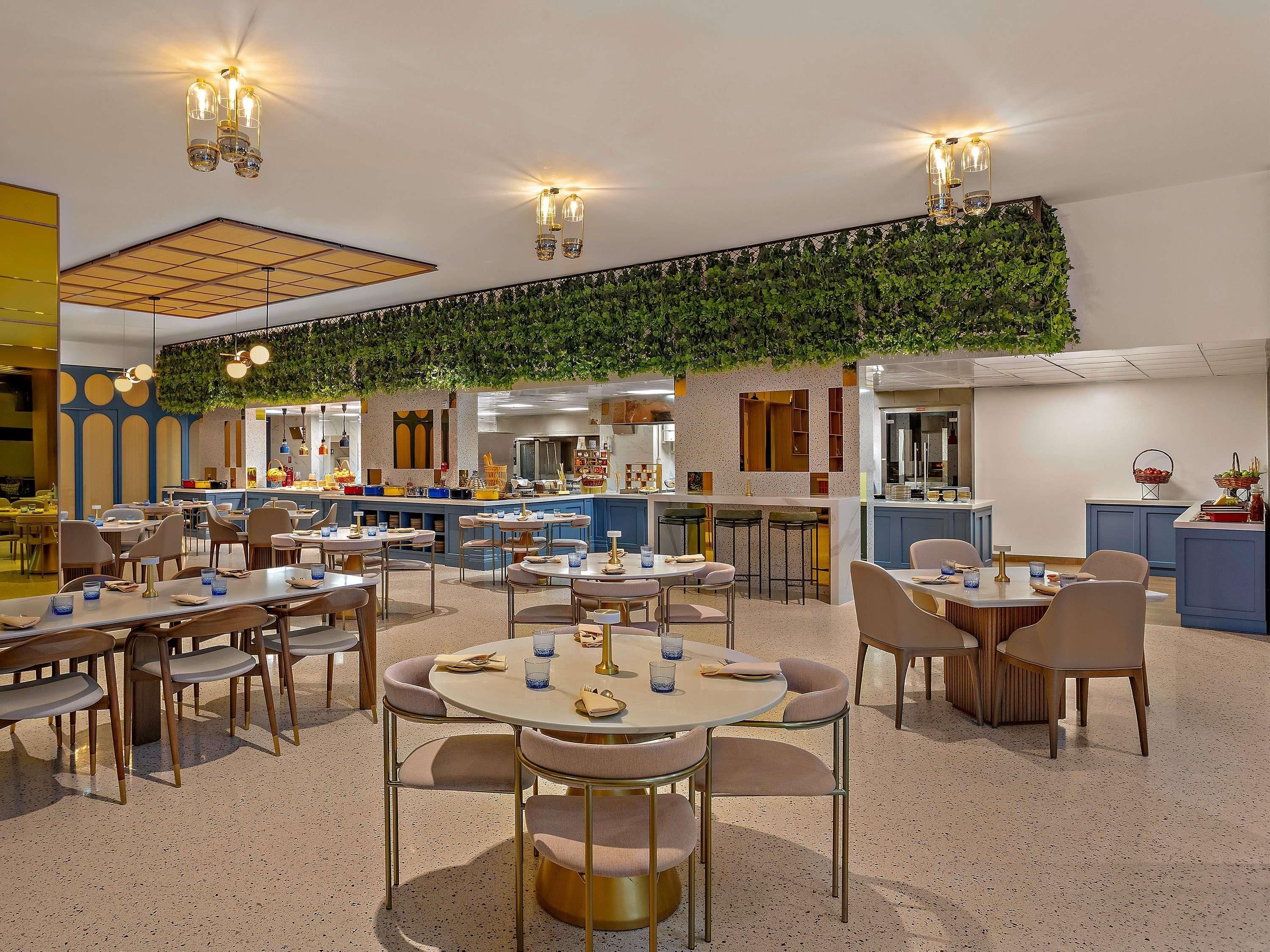 Un restaurant moderne avec des tables rondes, un bar et un mur végétal.