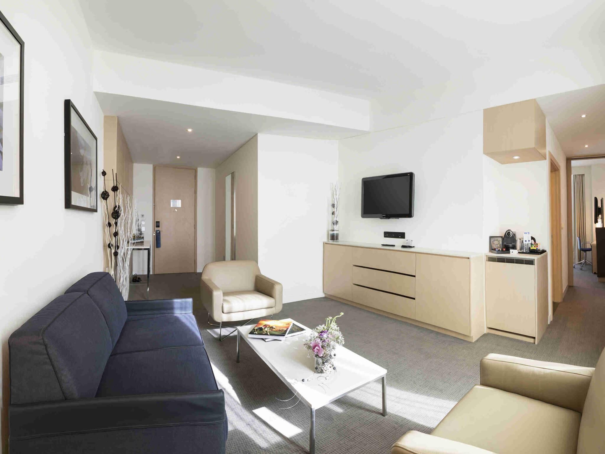 Een moderne woonkamer met een bank, fauteuil, salontafel, televisie en een kitchenette.