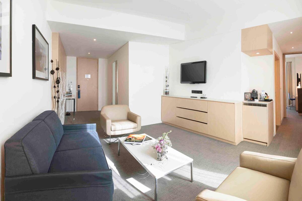 Een moderne woonkamer met een bank, fauteuil, salontafel, televisie en een kitchenette.