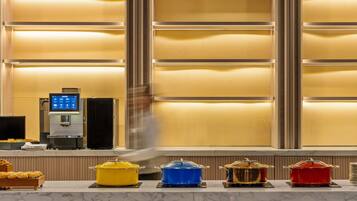 Una zona reception di un hotel con una macchina per caffè, uno schermo digitale e un buffet con diversi piatti.