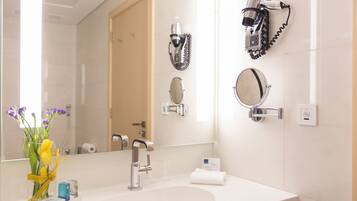 A hotel bathroom with a large mirror, a sink, and two hair dryers mounted on the wall.