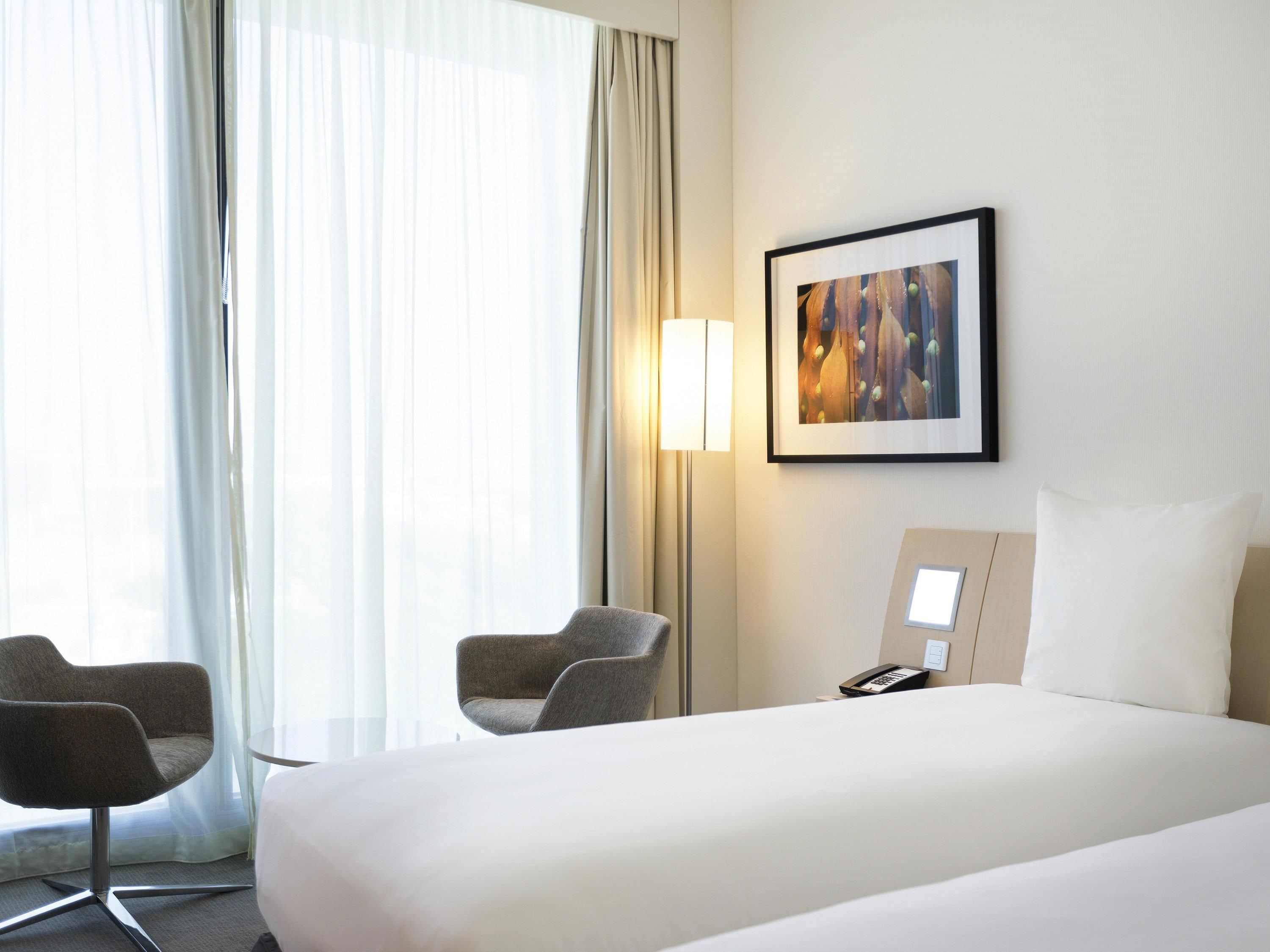 A hotel room with a bed, two armchairs, a bedside table with a lamp, a phone, and a framed picture on the wall.