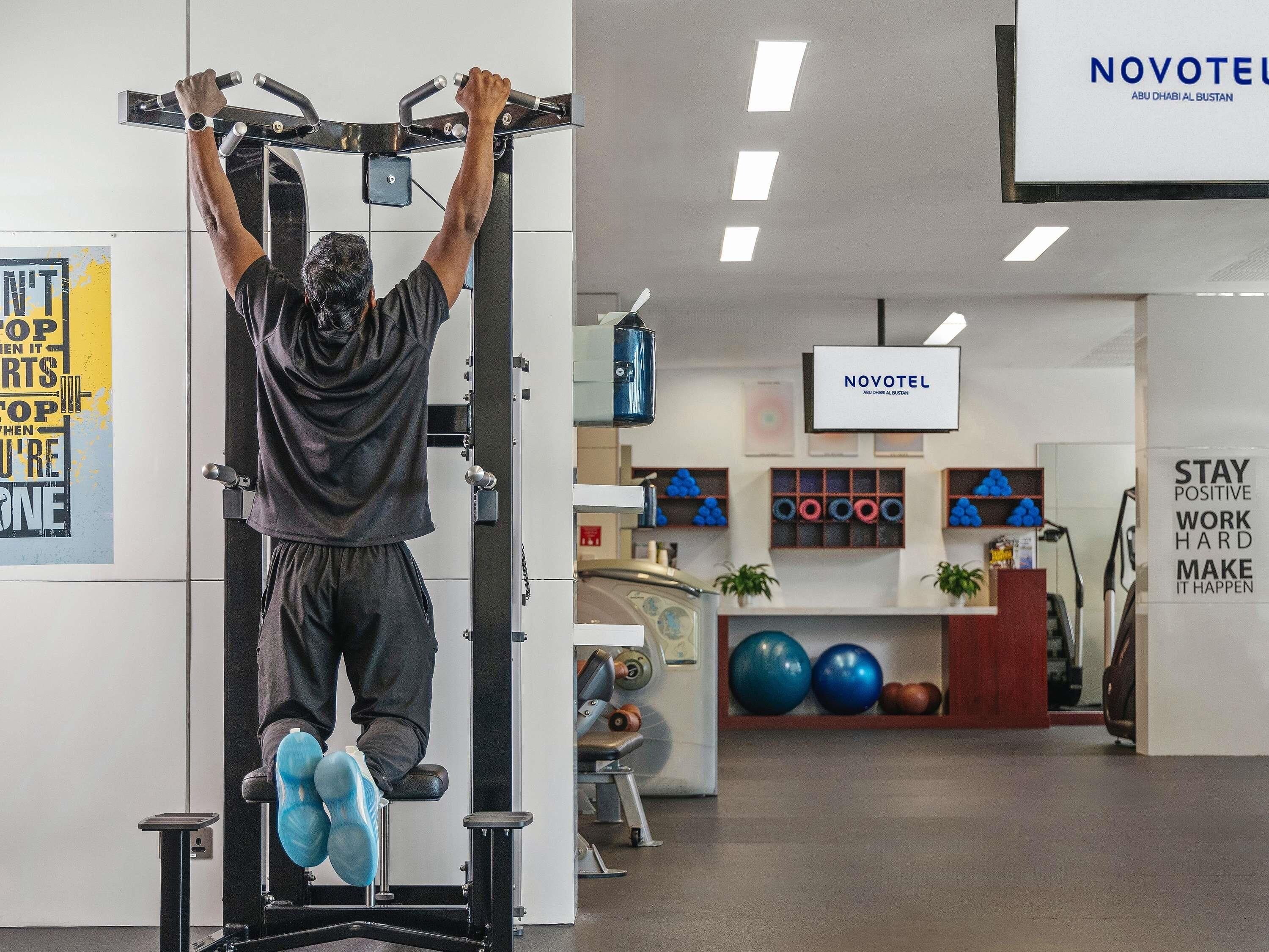 A person using a pull-up bar in a gym with a Novotel sign and motivational posters.