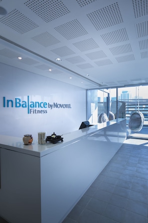 A modern fitness center with a reception desk, a large window, and a ceiling with a unique pattern.