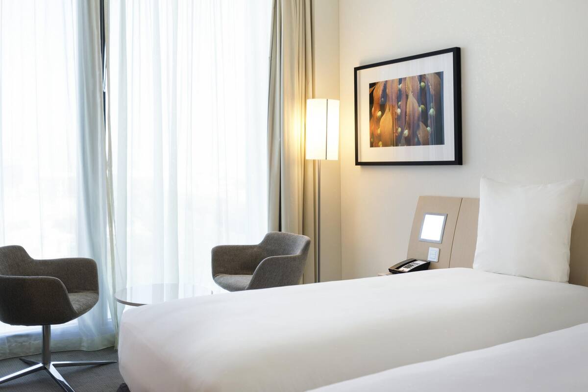 Hotelkamer met een bed, twee fauteuils, een nachtkastje met een lamp, een telefoon en een lijst op de muur.