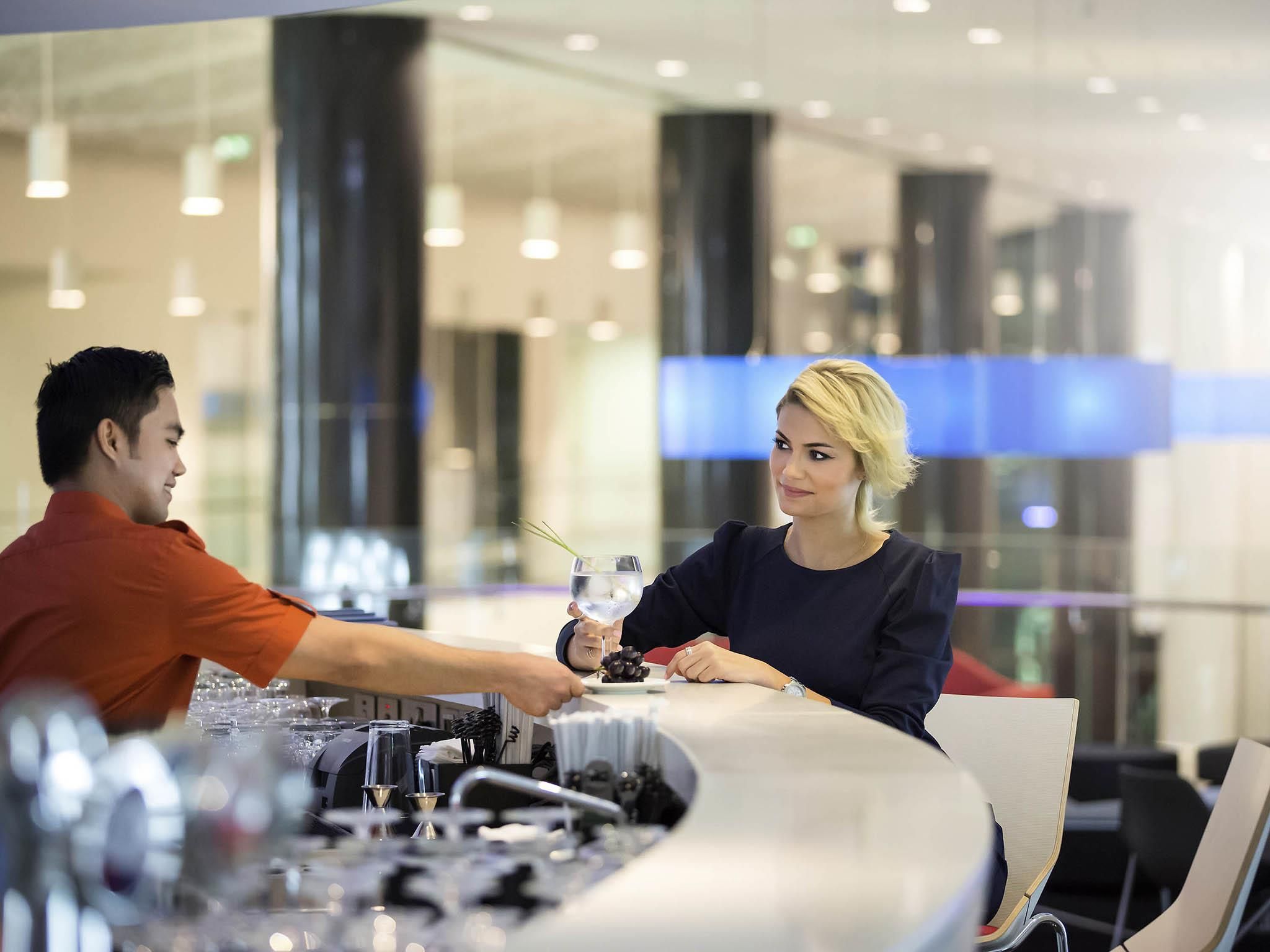 Un interior moderno con una zona de bar, separadores de vidrio y mobiliario contemporáneo.