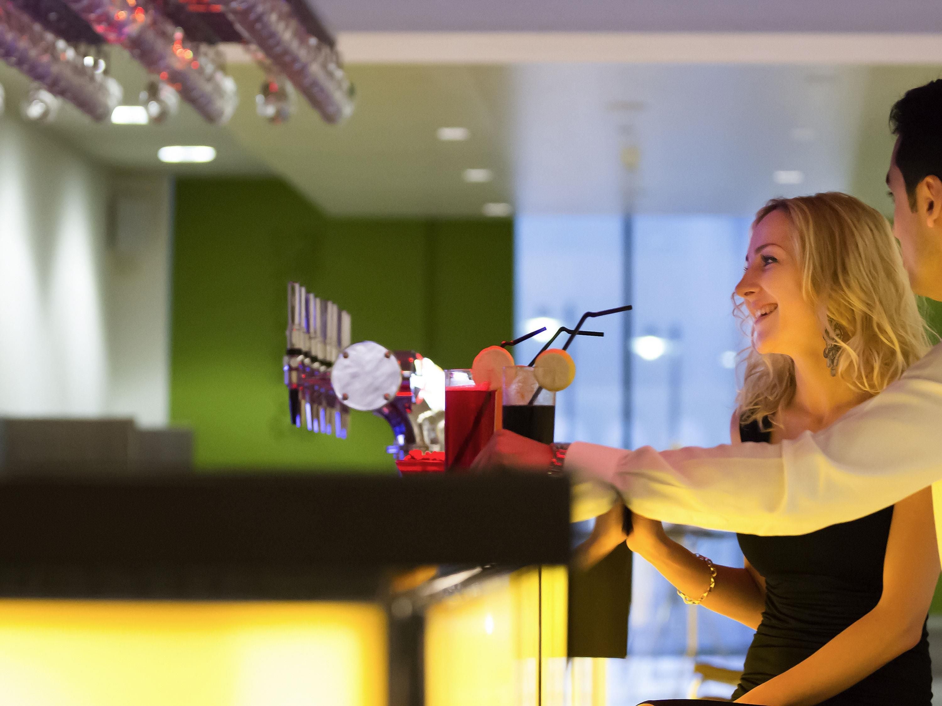 En bardisk med en bartender och en kund. Baren har en modern design med en grön vägg och en dekorativ lampa.