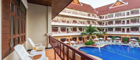 Un hotel con zona de piscina, varios balcones y un área de estar cubierta con sillas.