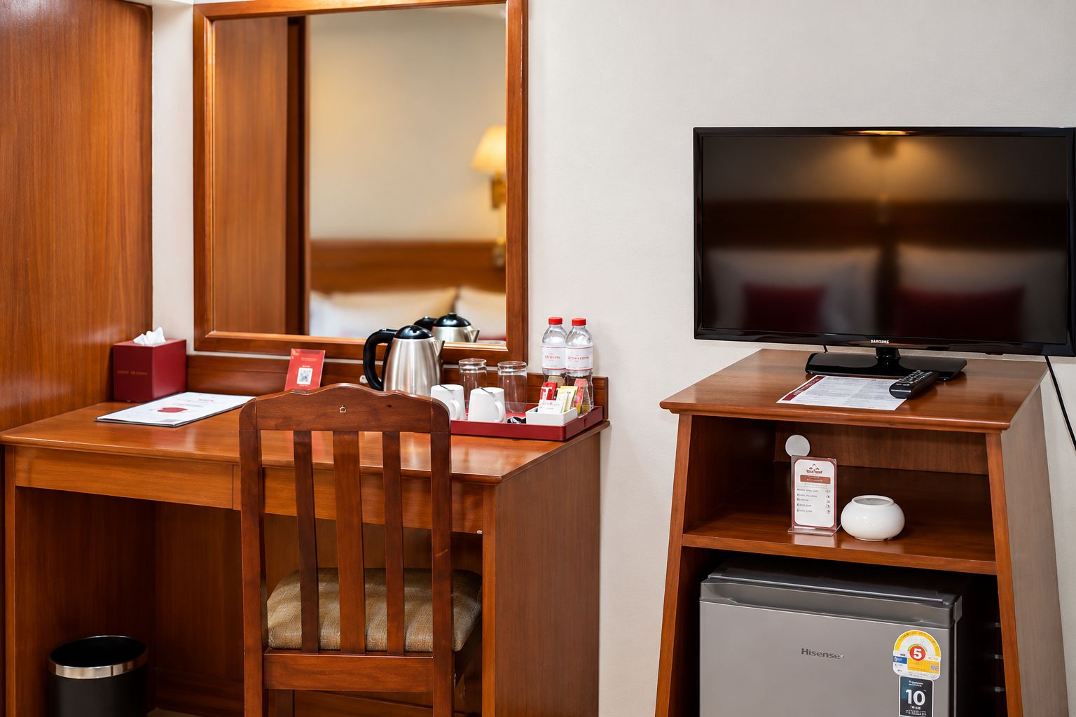 Een hotelkamer met een houten bureau, een televisie, een minibar en een kleine koelkast.