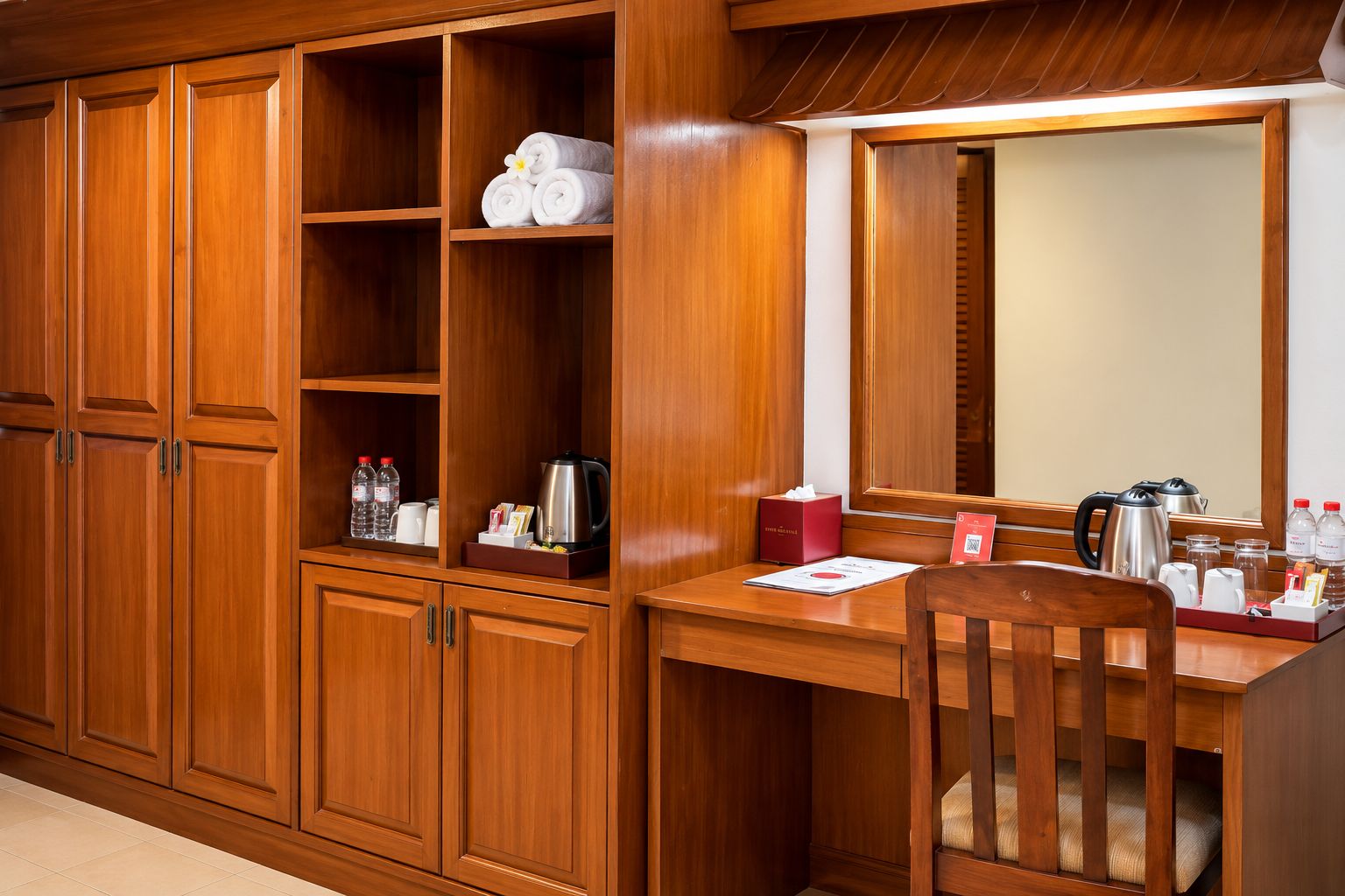 A wooden vanity with a mirror, a wooden desk with toiletries, and a chair.