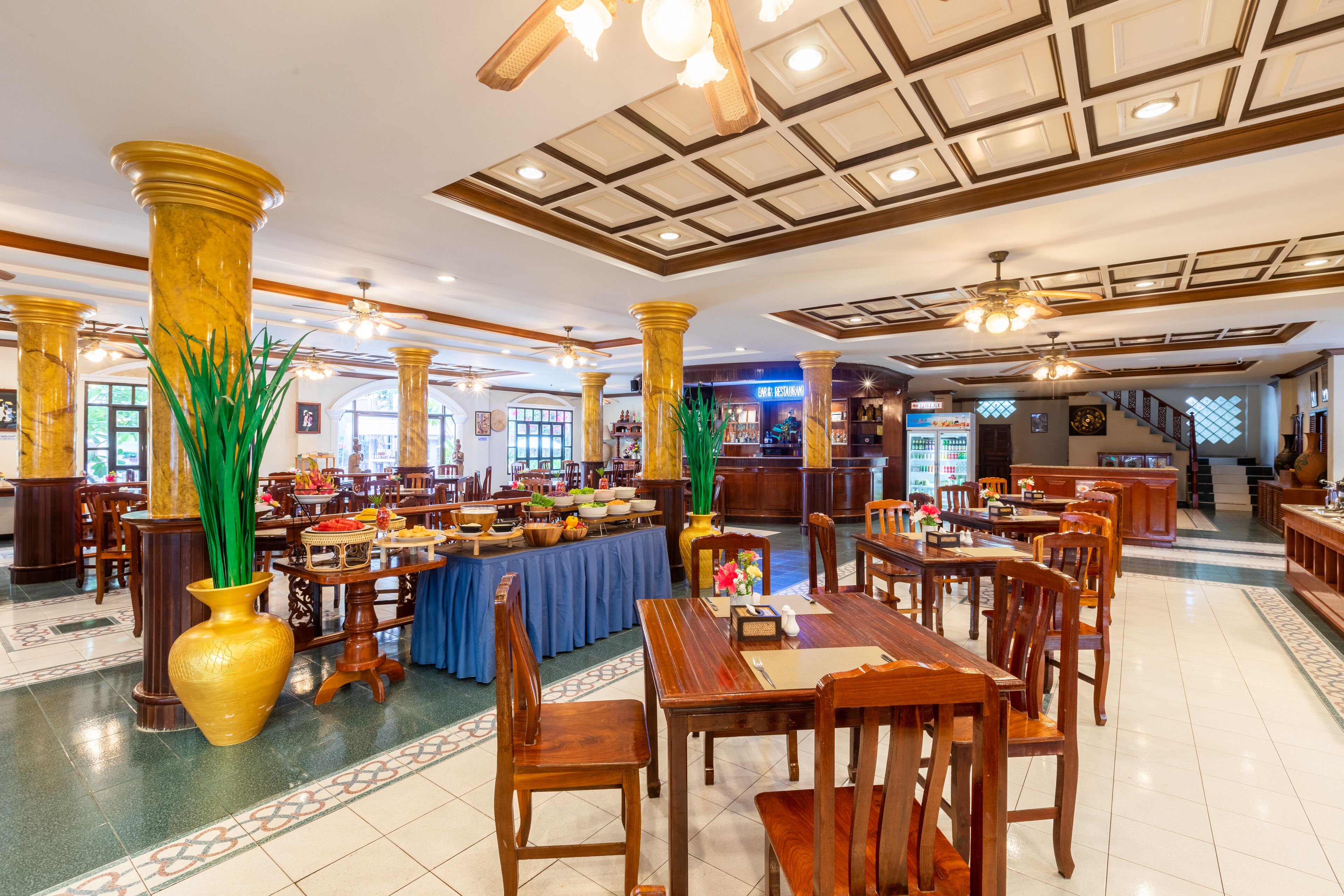 A spacious dining area with high wooden tables and chairs, a buffet setup, and a ceiling with a grid pattern.