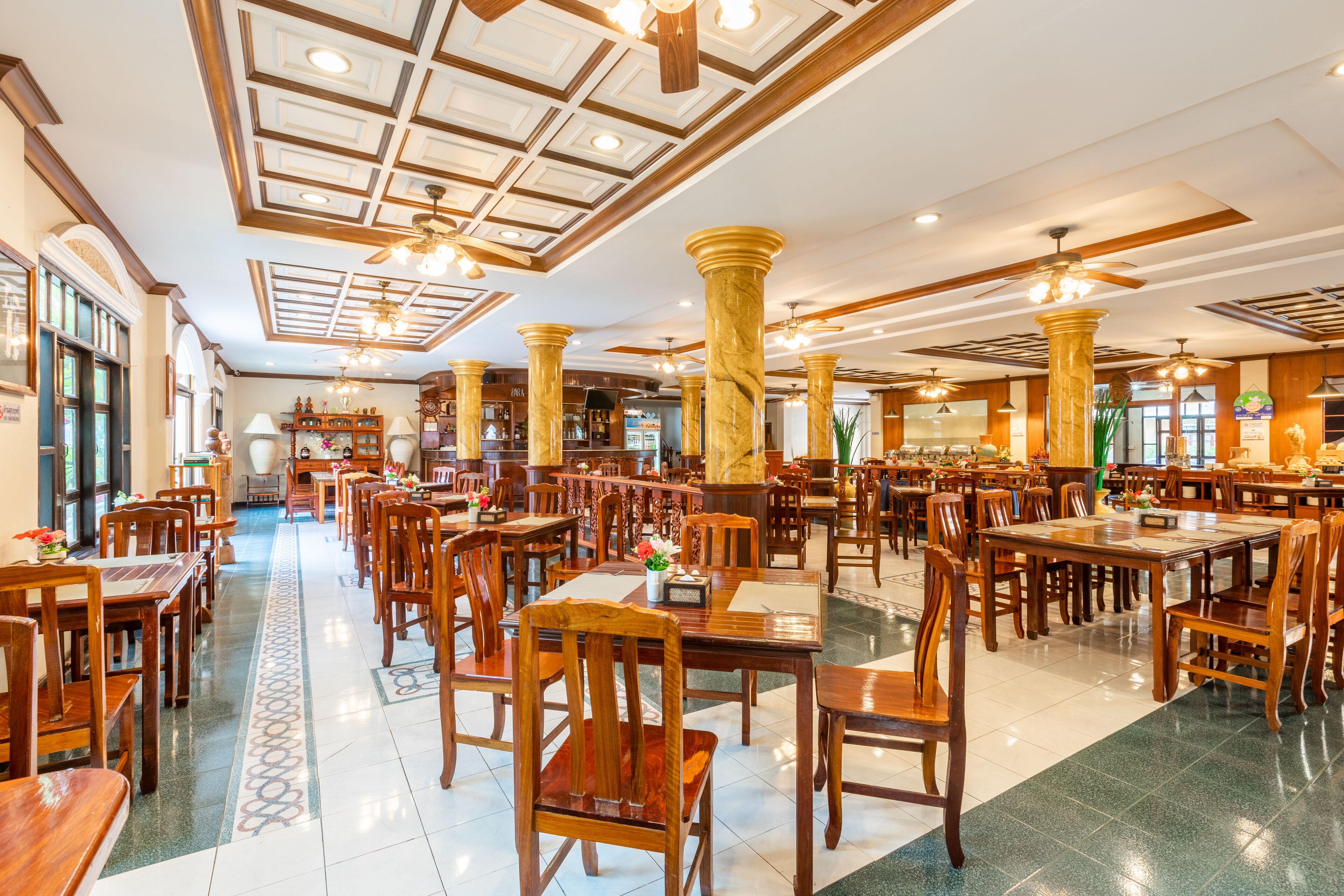A spacious dining area with wooden tables and chairs, marble columns, and a patterned floor.