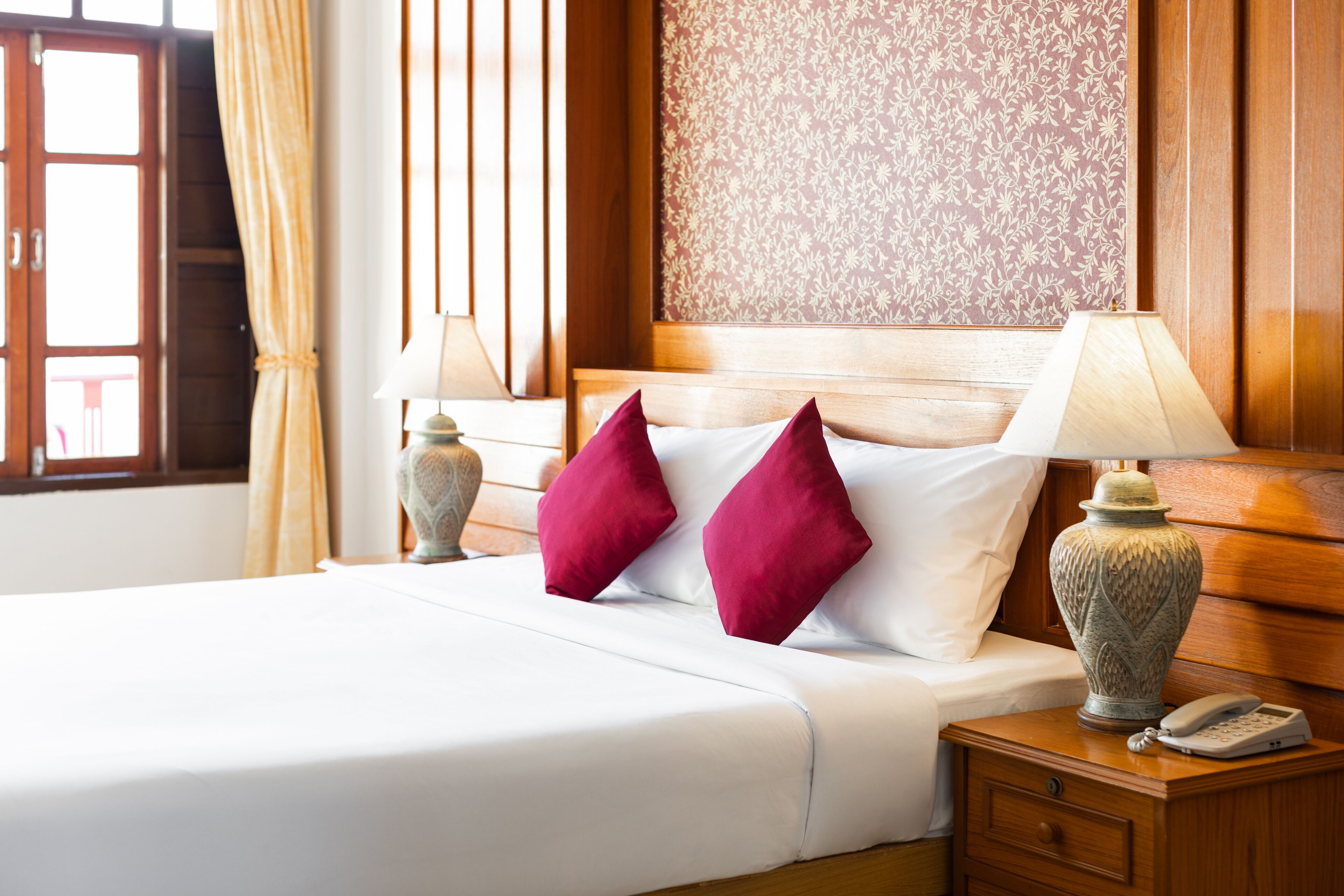 Habitación de hotel con cama, dos lámparas, una mesita de noche y papel tapiz estampado.