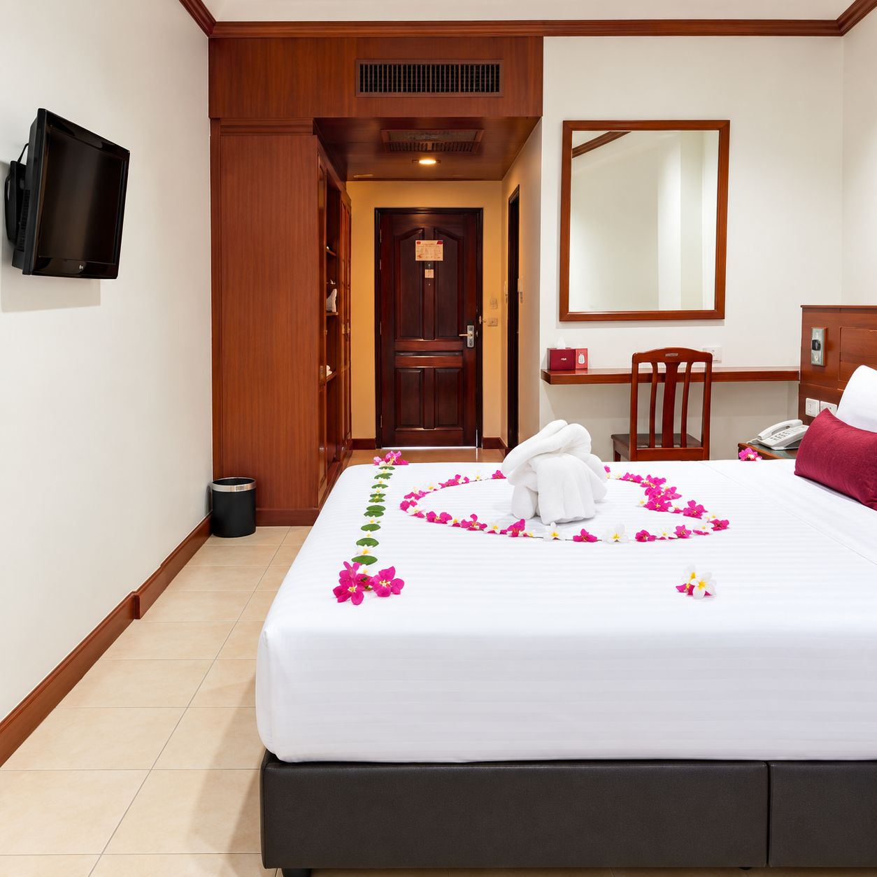 A hotel room with a bed, a desk, a chair, a TV, and a door leading to another room.