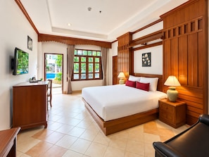A hotel room with a large bed, a desk, a chair, a TV, and a view of a swimming pool. - Tony Resort (Patong)