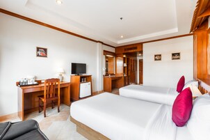 Habitación de hotel con dos camas, un escritorio con silla, televisión y un refrigerador pequeño.