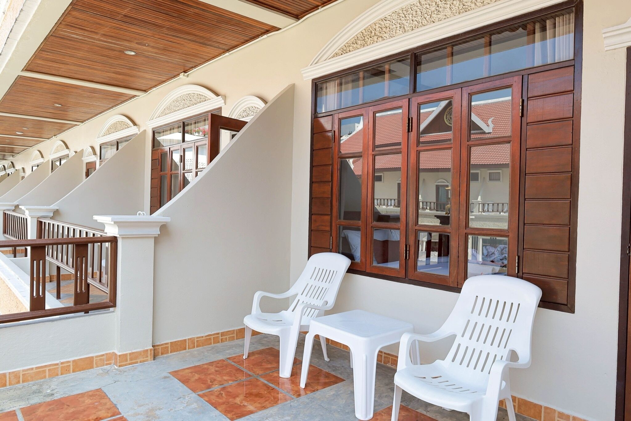 A balcony with white plastic chairs and a small table, wooden railings, and a tiled floor.