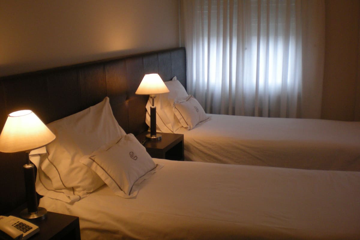 Una habitación de hotel con dos camas, cada una con una lámpara de noche y un teléfono en la mesita.