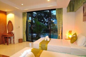 Habitación de hotel con dos camas, un ventanal con vistas a una piscina y palmeras, una silla de madera y una mesita.