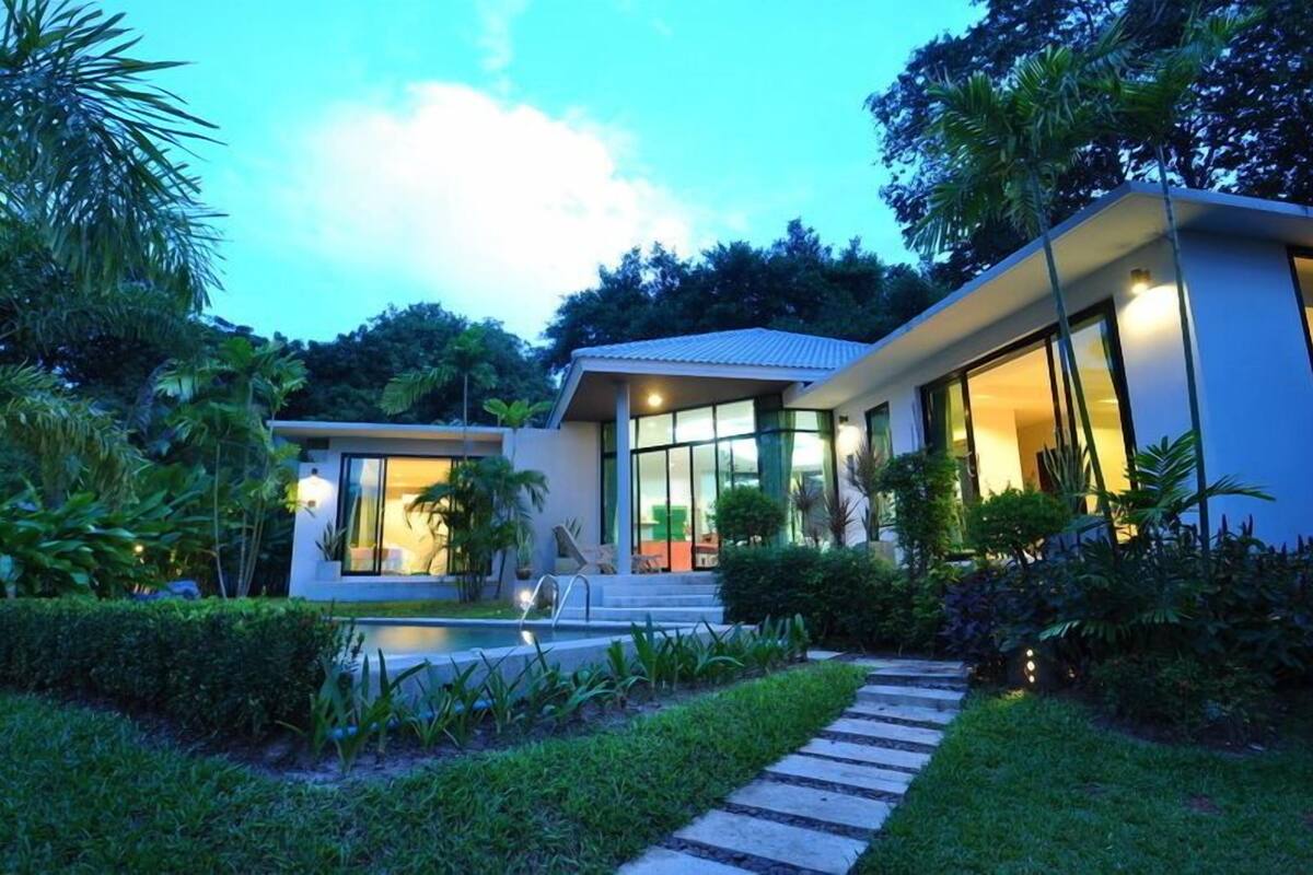 Uma casa moderna com piscina, rodeada por vegetação exuberante.