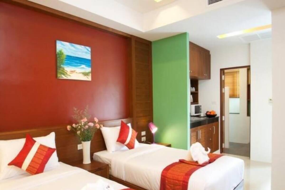 Quarto de hotel com duas camas, um quadro na parede, uma parede de destaque verde e vista para a cozinha.