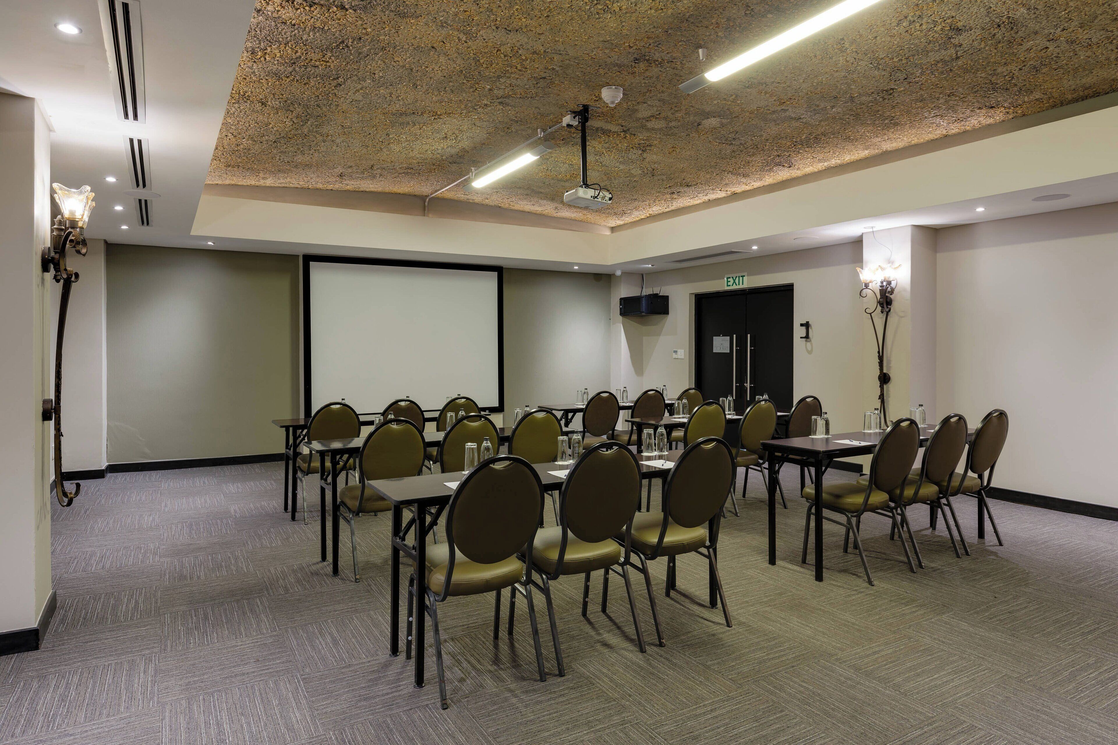 Una sala conferenze con un proiettore, uno schermo e diversi tavoli con sedie.