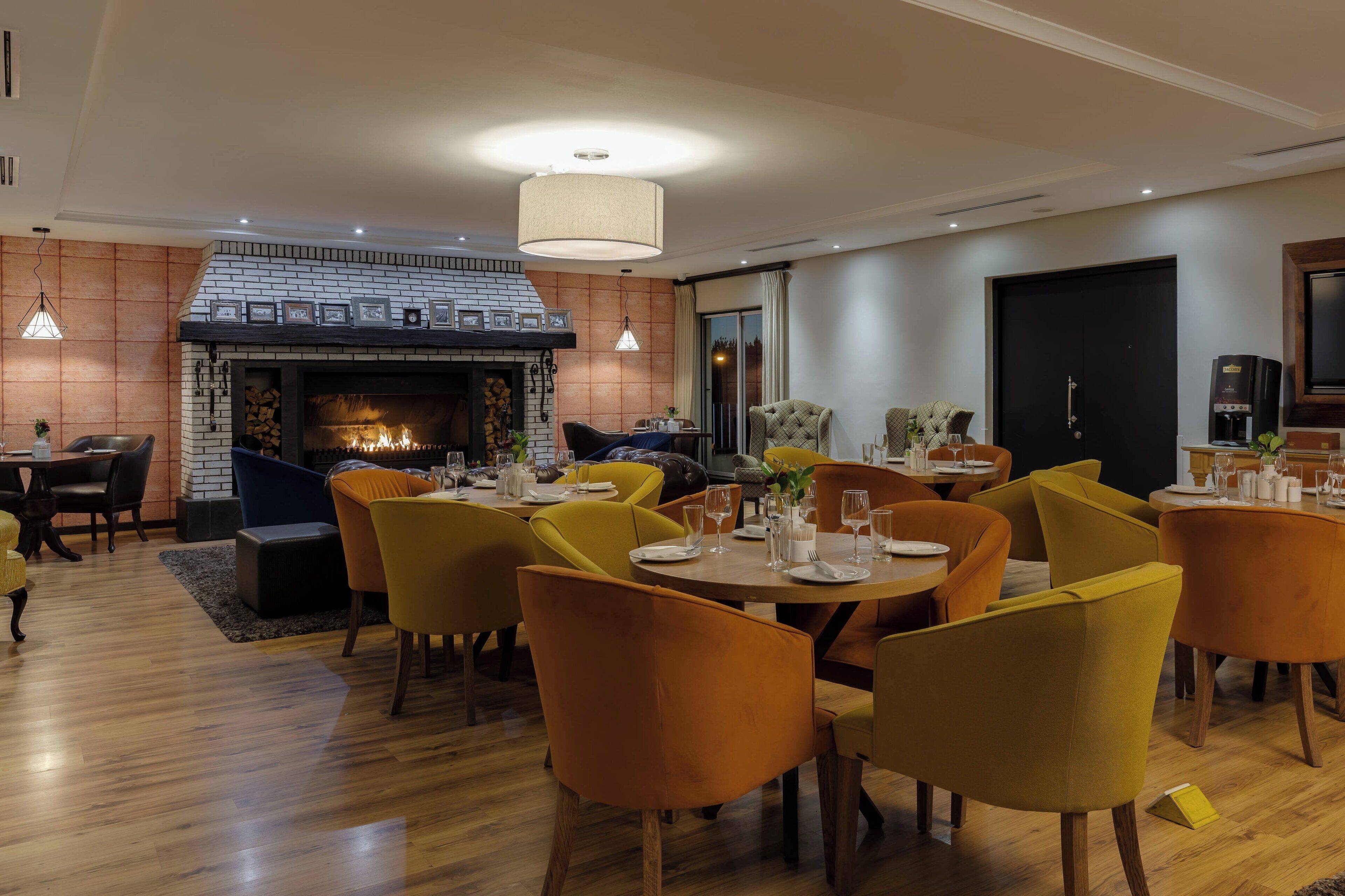 A modern dining area with a fireplace, wooden flooring, and orange chairs.