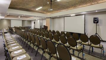 Un salón de conferencias con filas de sillas, un proyector y una pantalla.