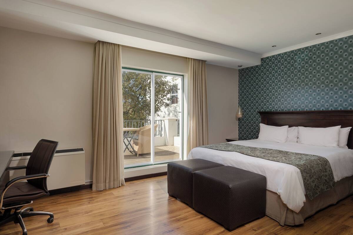 Ein Hotelzimmer mit einem großen Bett, einem Schreibtisch und Blick ins Freie durch eine Schiebetür.