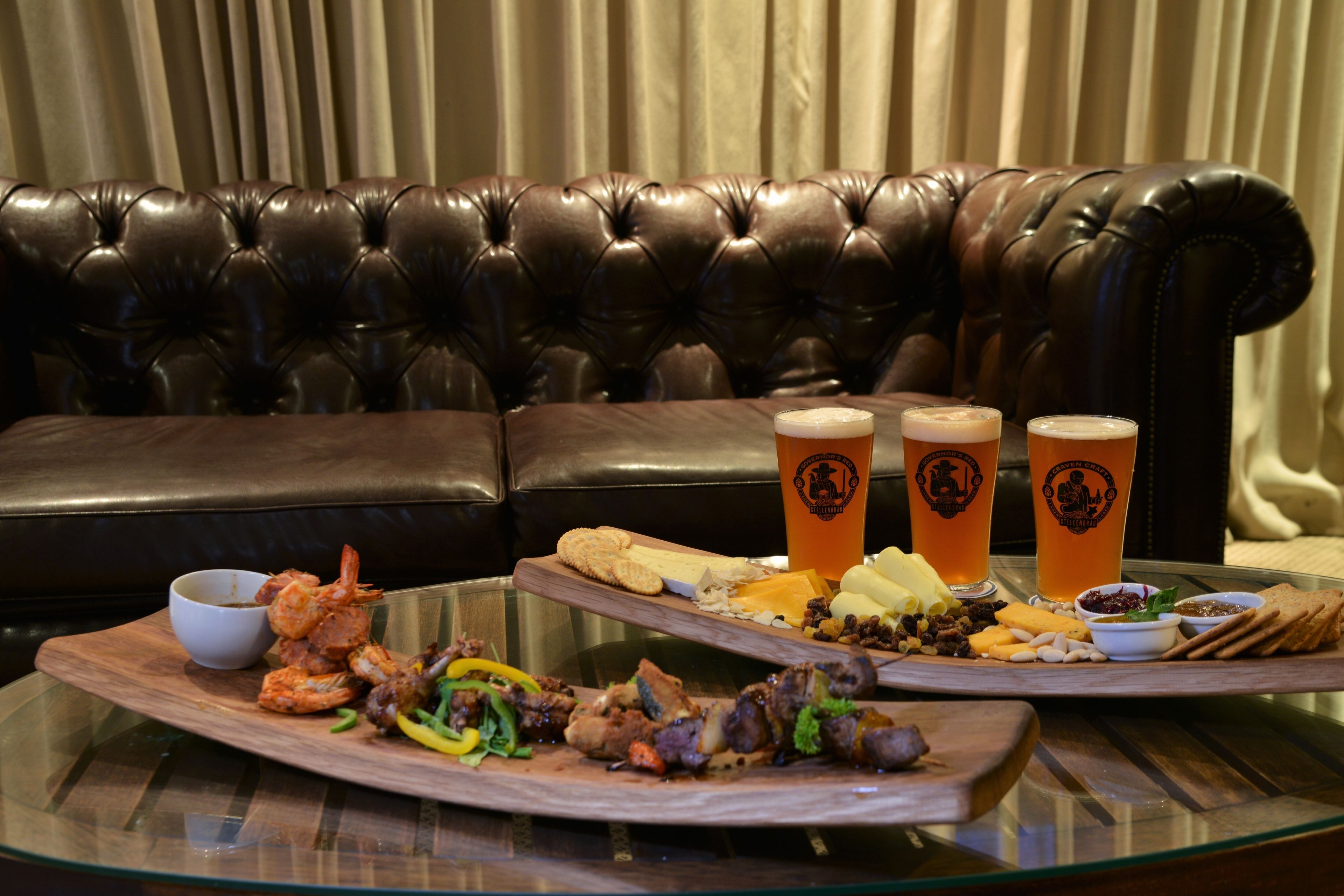 A dining table with a variety of food and drinks, a leather couch in the background, and a glass partition.