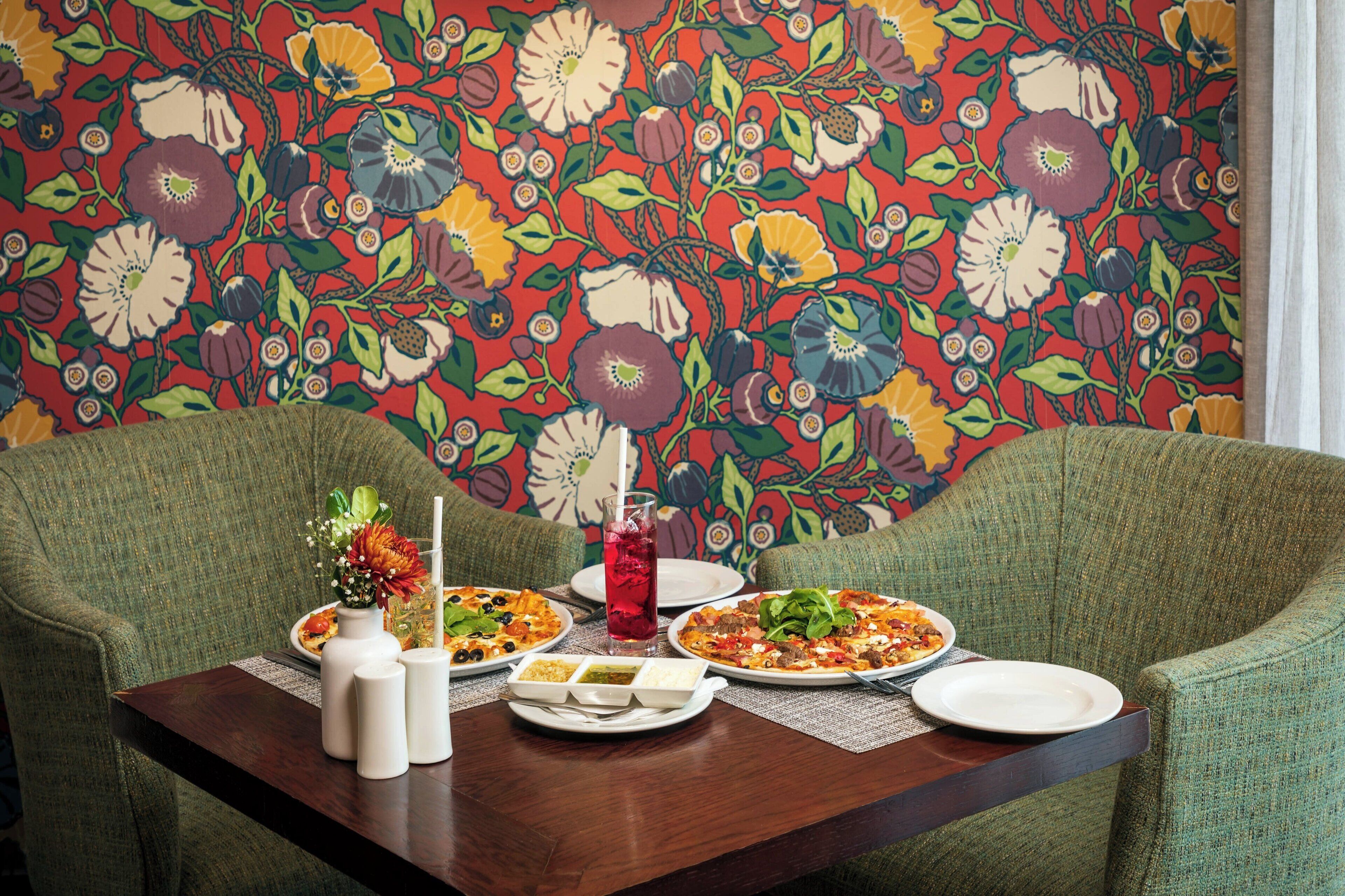 A dining table with two plates of food, a vase with flowers, and a glass of red drink.