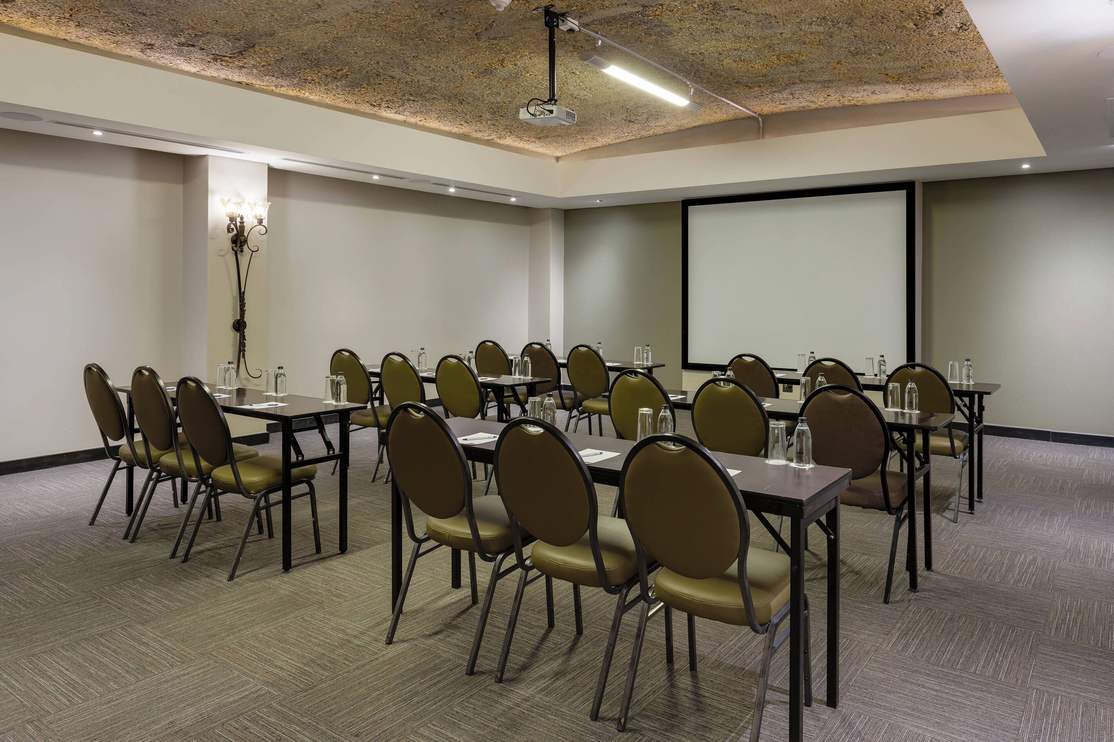 A conference room with multiple tables and chairs, a projector screen, and a large screen on the wall.