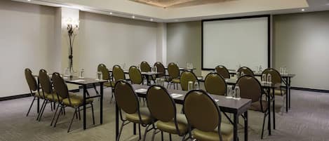 A conference room with multiple tables and chairs, a projector screen, and a large screen on the wall.