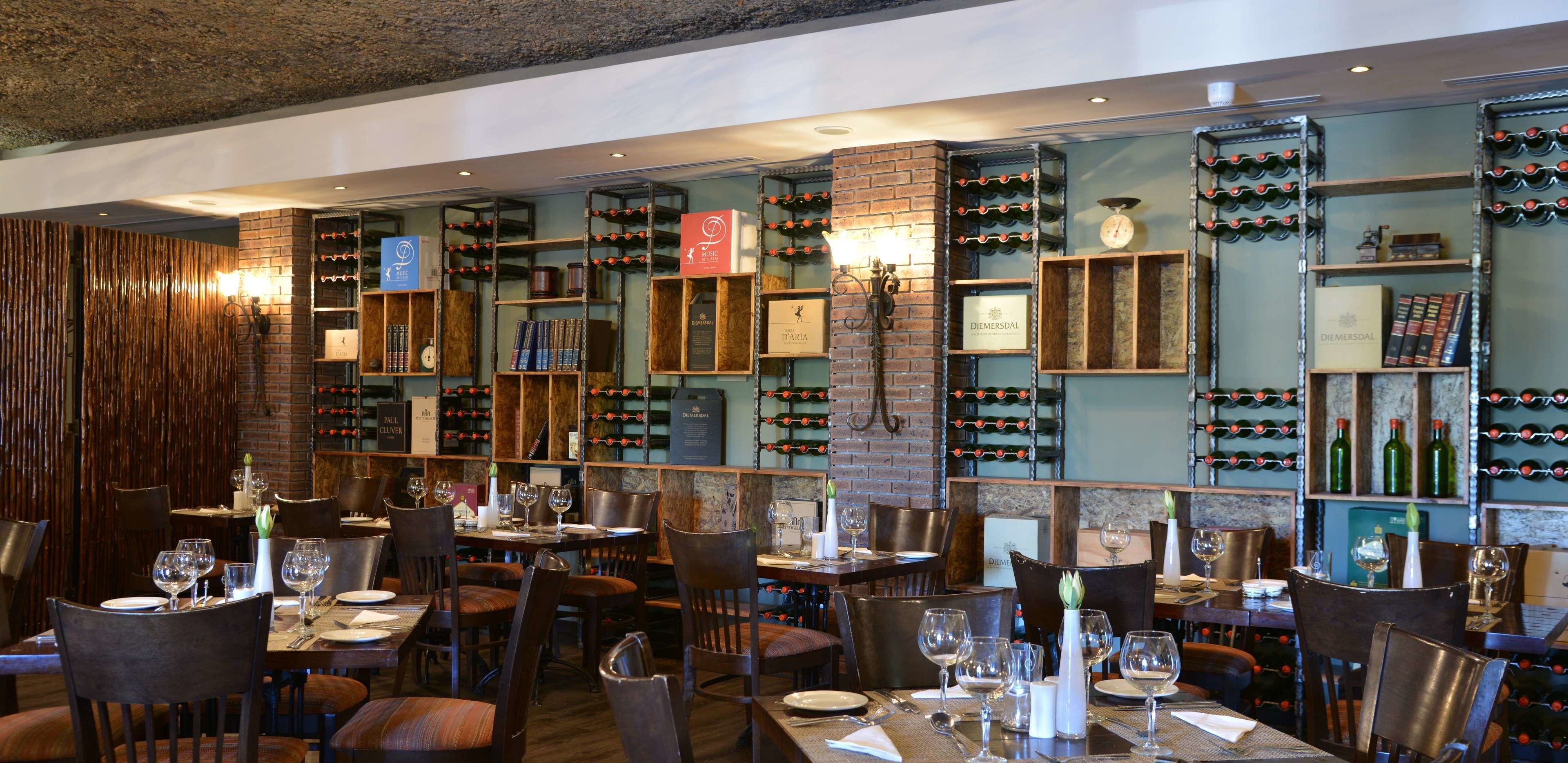 L’intérieur d’un restaurant présente de nombreuses tables, des chaises, des étagères à vin et des rayons où sont exposées des bouteilles de vin et des livres.