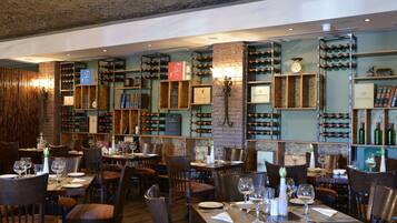 L’intérieur d’un restaurant présente de nombreuses tables, des chaises, des étagères à vin et des rayons où sont exposées des bouteilles de vin et des livres.