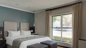 A modern hotel room with a large bed, two bedside tables, a small table, and a large window with curtains.