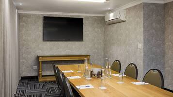 A conference room with a long wooden table, chairs, a flat-screen TV, and an air conditioning unit.