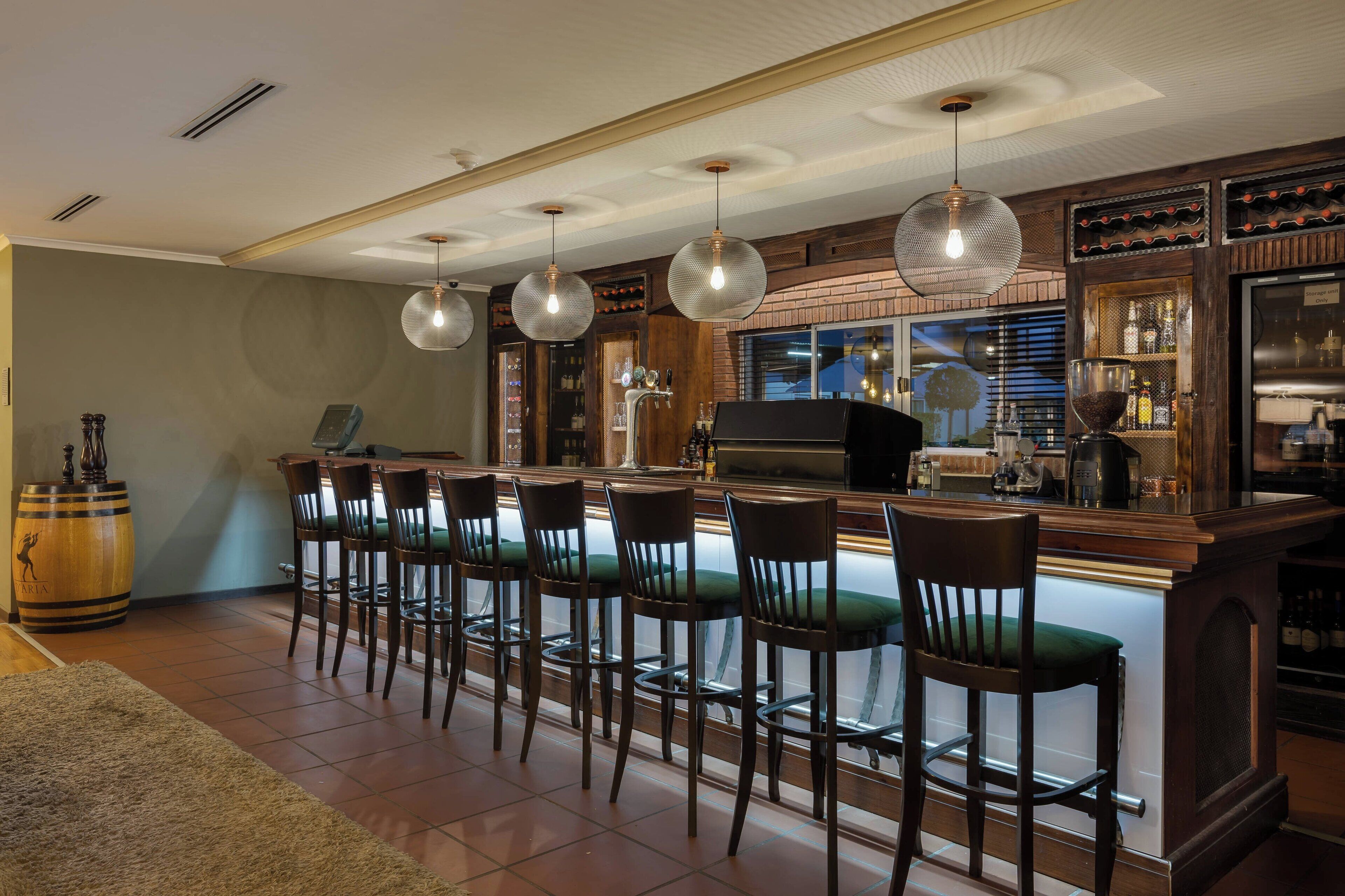 Uma área de bar com um balcão comprido, vários banquetas e luminárias pendentes.