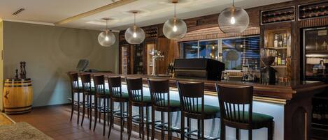 Uma área de bar com um balcão comprido, vários banquetas e luminárias pendentes.