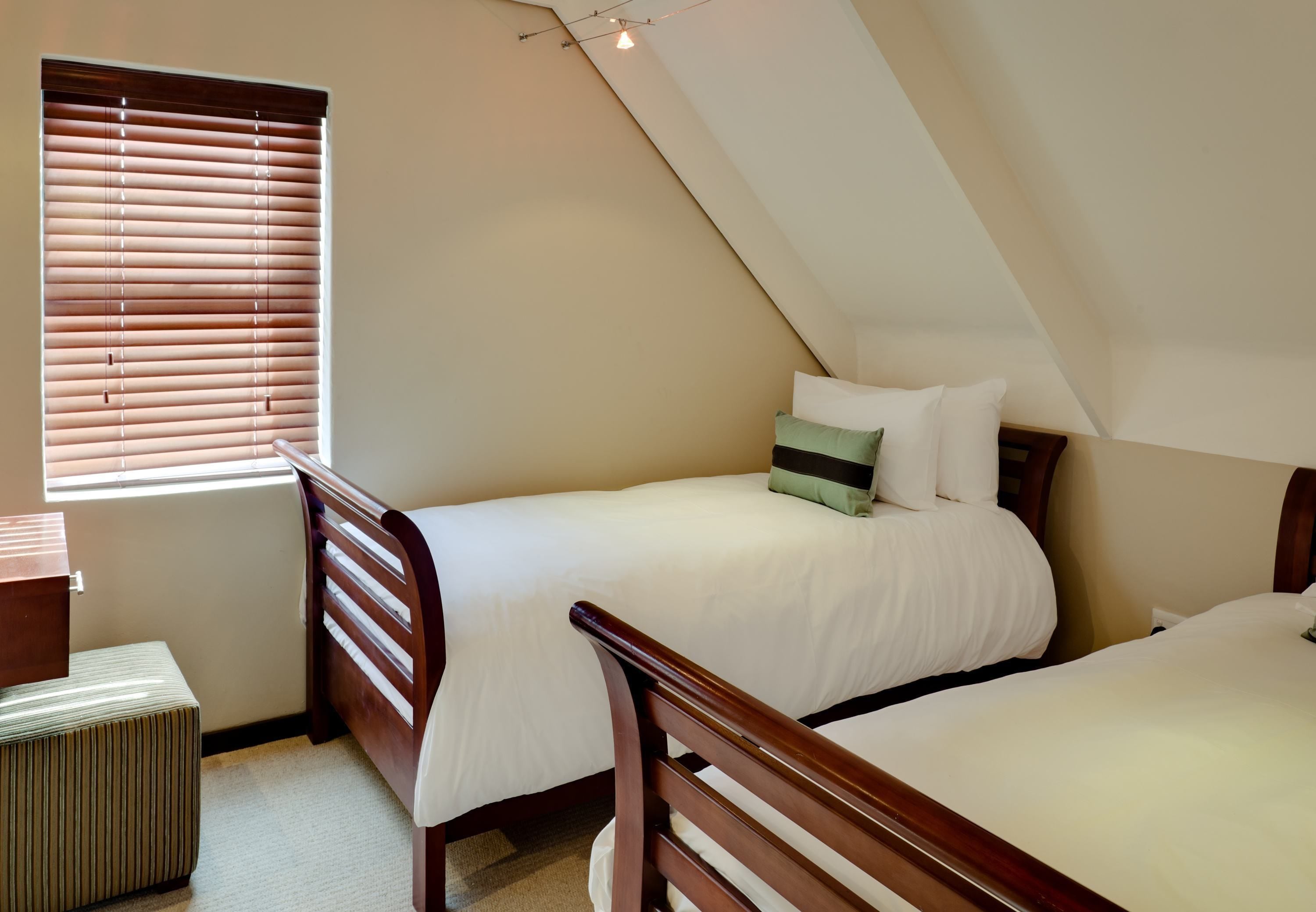 Een slaapkamer met twee éénpersoonsbedden, een raam met zonwering, een nachtkastje en een prullenbak.