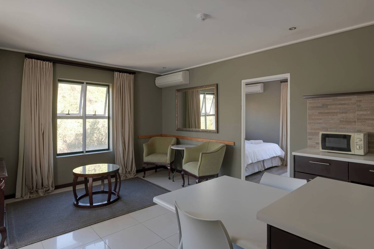 Ein Hotelzimmer mit einem Bett, einem Esstisch, zwei Sesseln, einem kleinen runden Tisch, einer Mikrowelle und einer Klimaanlage.