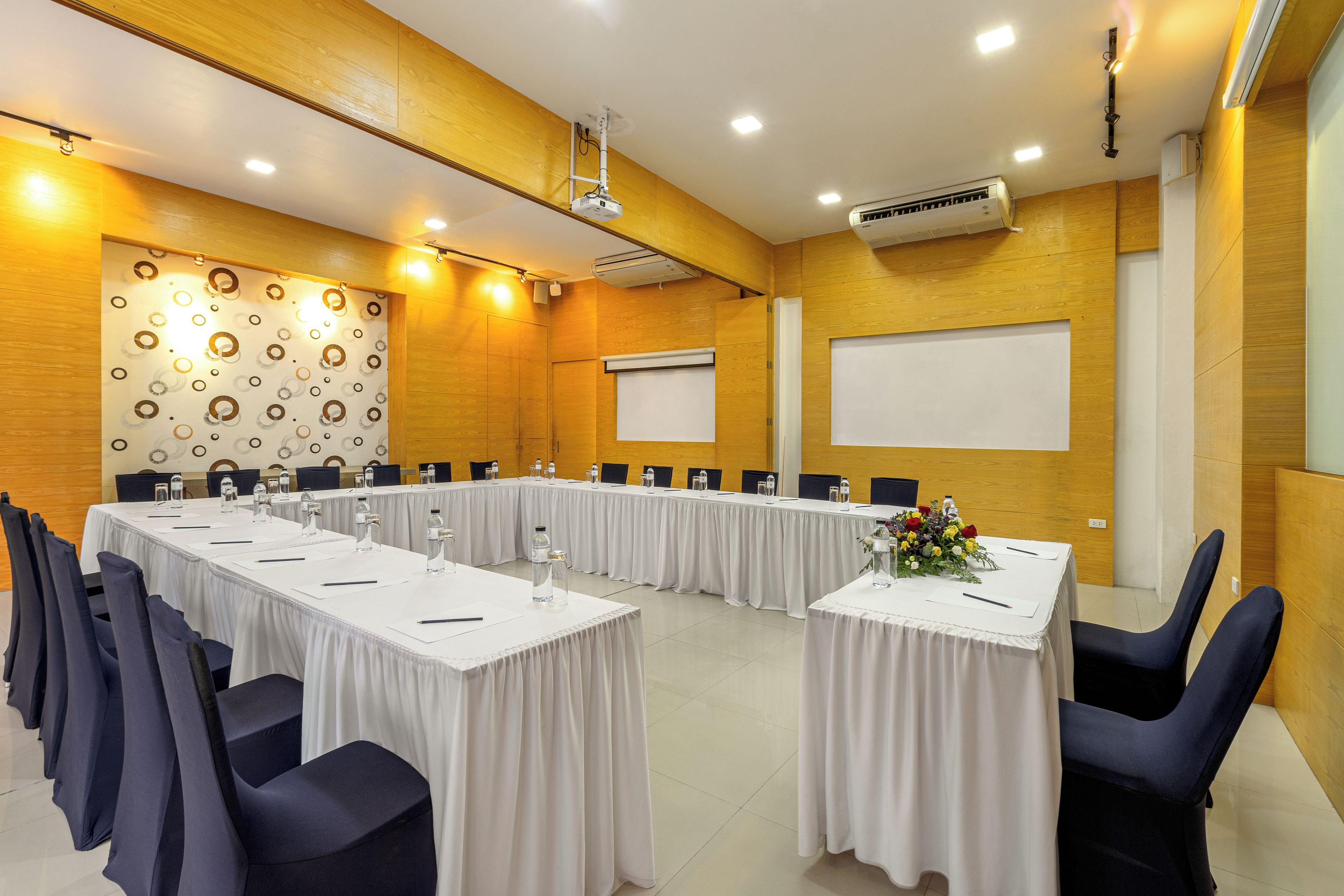 A conference room with long tables, chairs, a projector, and a whiteboard.